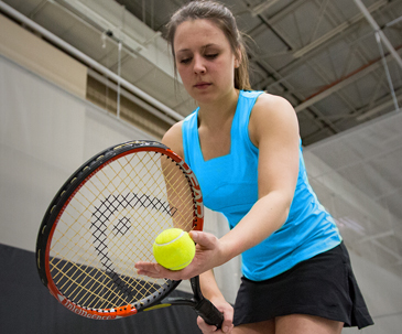 Player holding a tennis racket and ball in the fieldhouse at SentryWorld