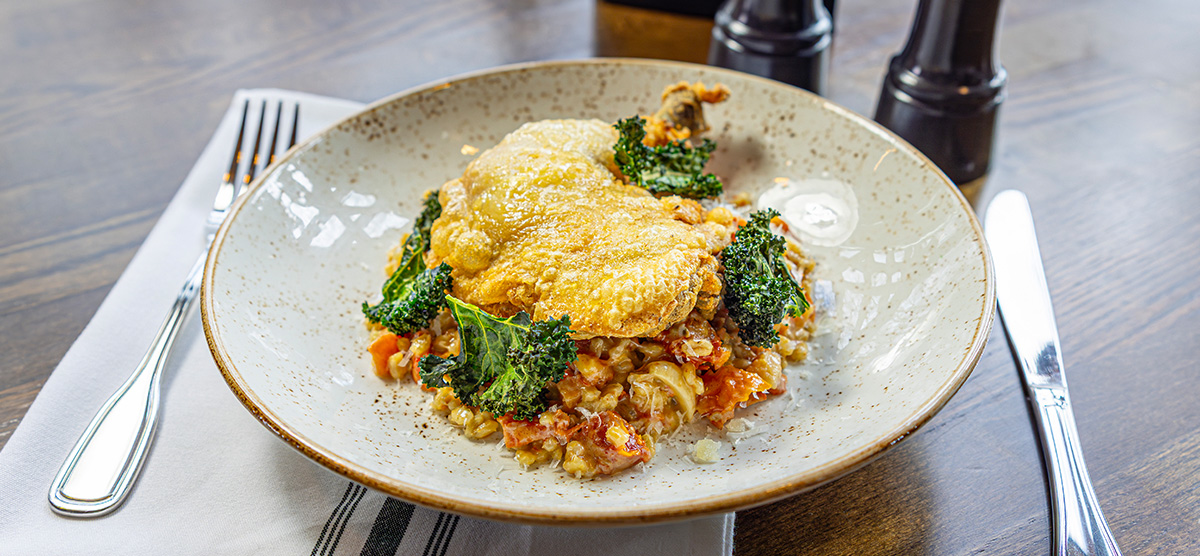 Chicken Confit with barley and sun-dried tomato risotto, kale chips, and aged Parmesan.