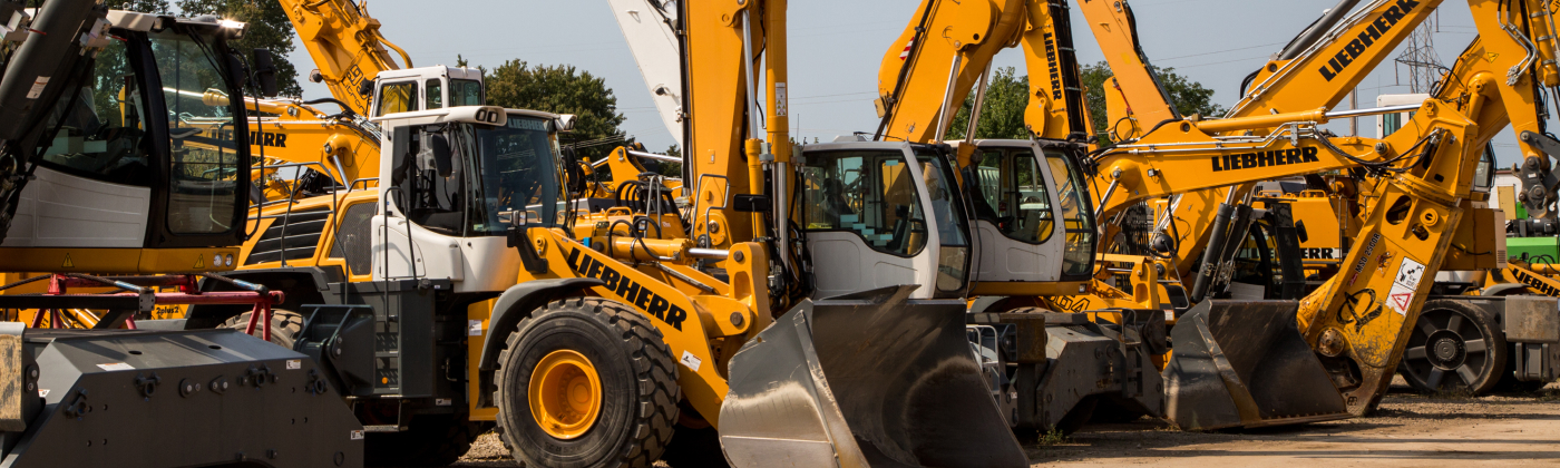 Row of yellow construction vehicles, including excavators and wheel loaders, parked outdoors.