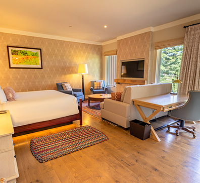 hero-lodging-rooms-396x364 Hotel room with one king sized bed and seating area in front of a fireplace.
