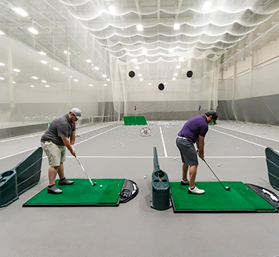 Two golfers hitting off practice mats in the indoor range at SentryWorld