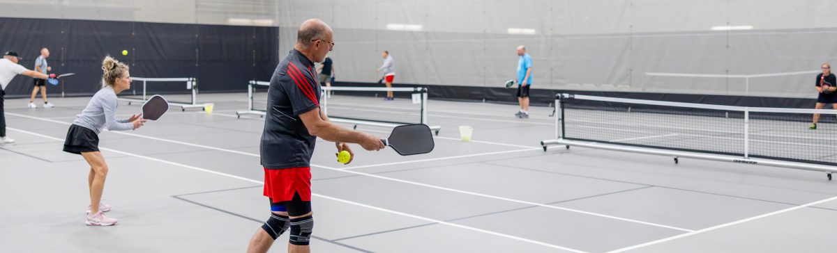 Multiple pickleball players warm up in the SentryWorld fieldhouse.