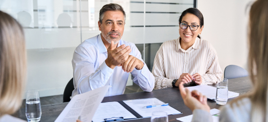 Business professionals engaged in a meeting, with a man speaking and a woman smiling.