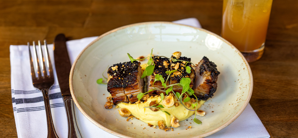 Plate of pastrami-spiced pork belly, orange-scented parsnip, and toasted hazelnuts.