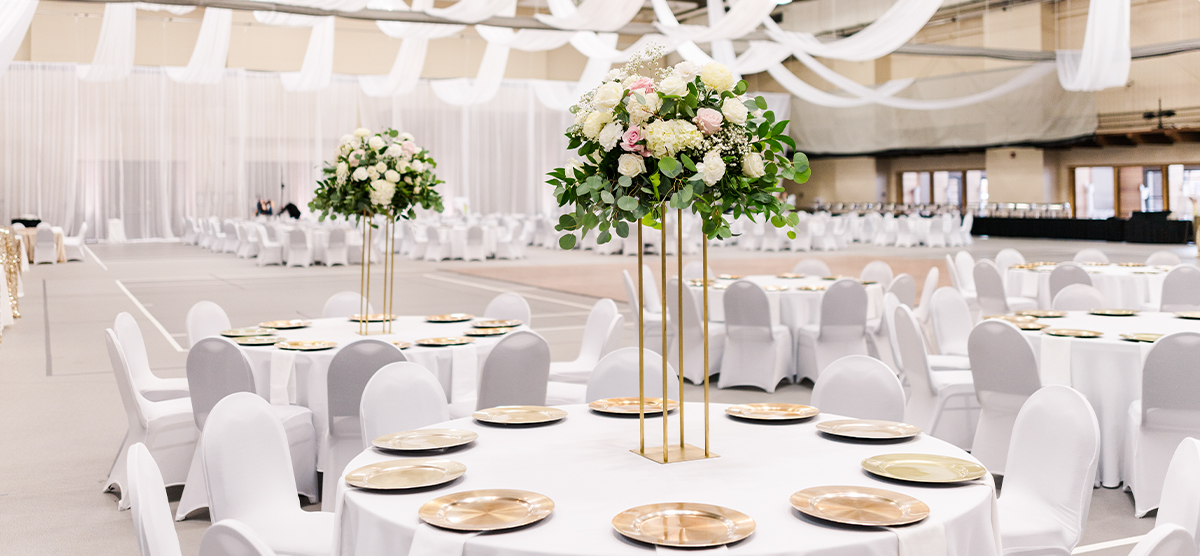 Round tables and floral centerpieces in the fieldhouse for a wedding reception