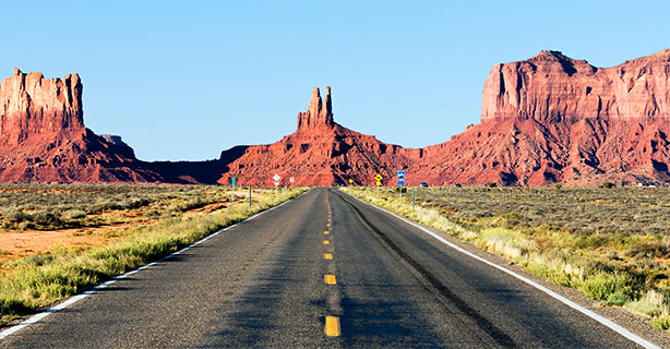 Two-lane highway with sandstone buttes in the distance.