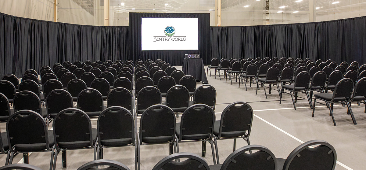 Rows of chairs and a projector screen set for a corporate meeting in the fieldhouse at SentryWorld