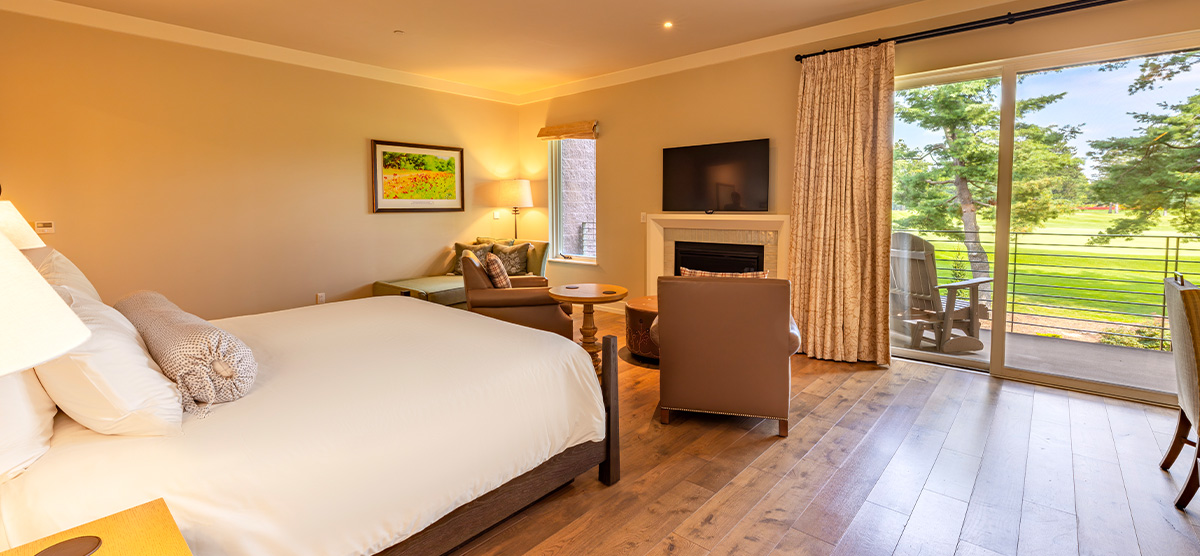 carousel-suite-golf-view-luxury-junior-1-1200x556 King bed with seating area, desk, and patio door overlooking the golf course.
