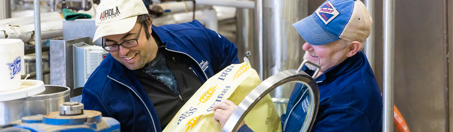 Two people putting beer ingredients in to make beer