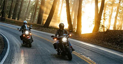 Two motorcycles riding on a two-lane road at sunset