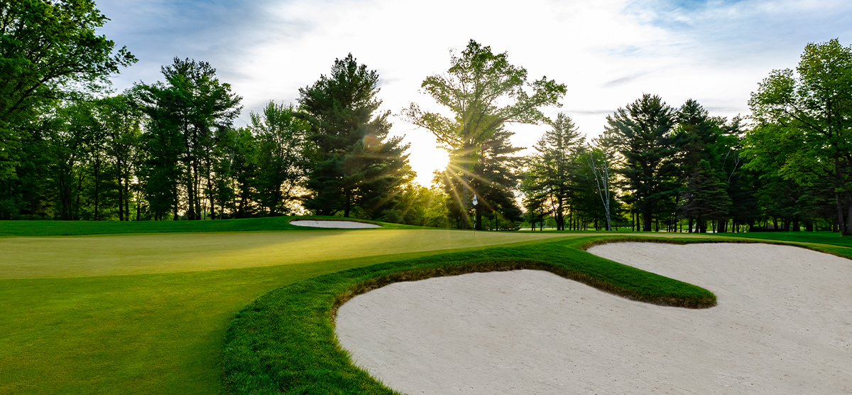 Sunshine peaking through trees onto a sand trap and putting green at SentryWorld