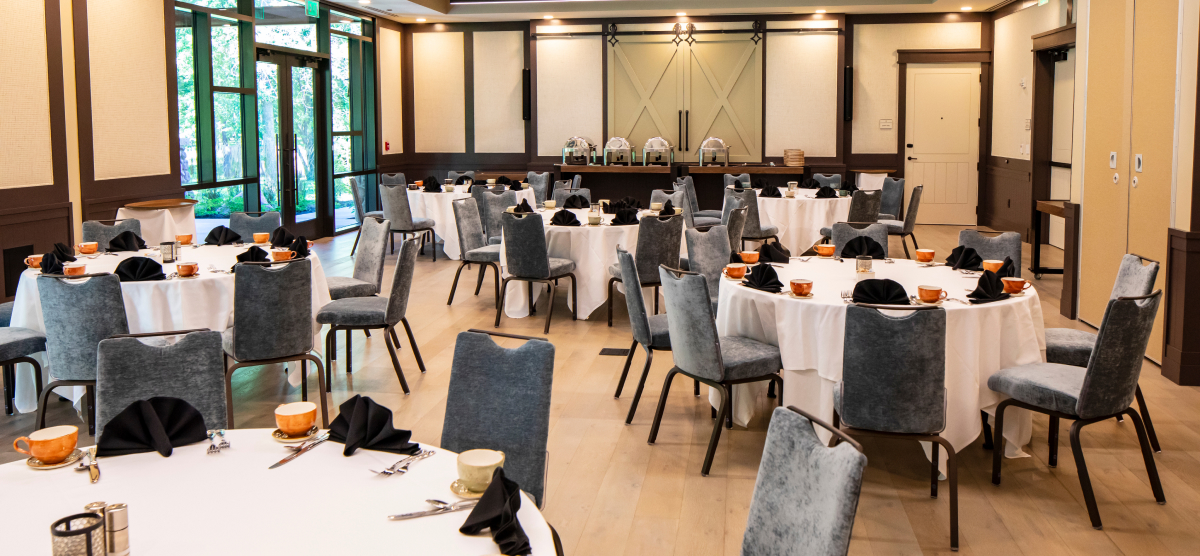 Event room with many round tables set with grey chairs, black napkins, and orange coffee mugs.