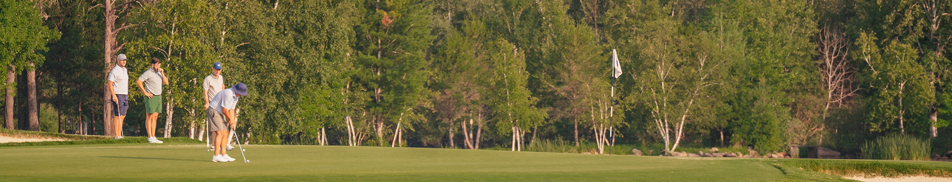 Man preparing to putt on a SentryWorld green while three friends watch on. 