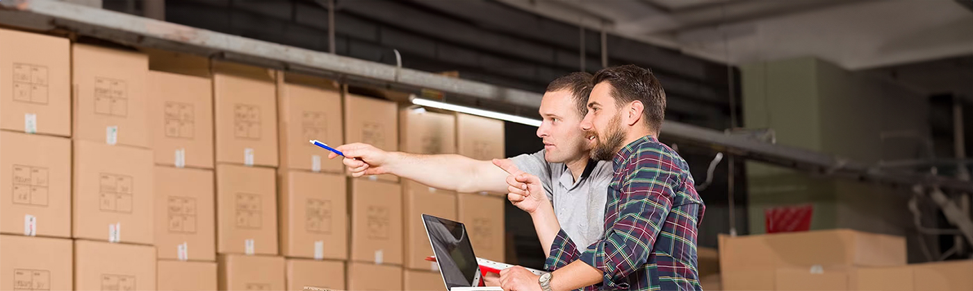 Two men with laptop pointing at something in warehouse