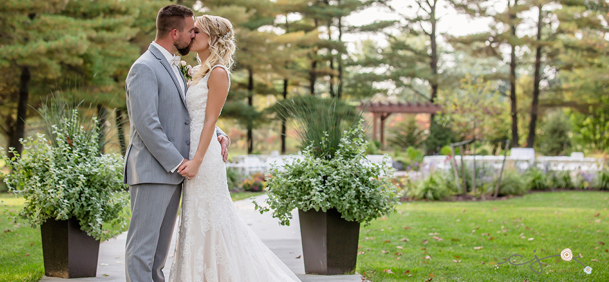 Bride and groom kissing on the aisle in front of the SentryWorld pergola