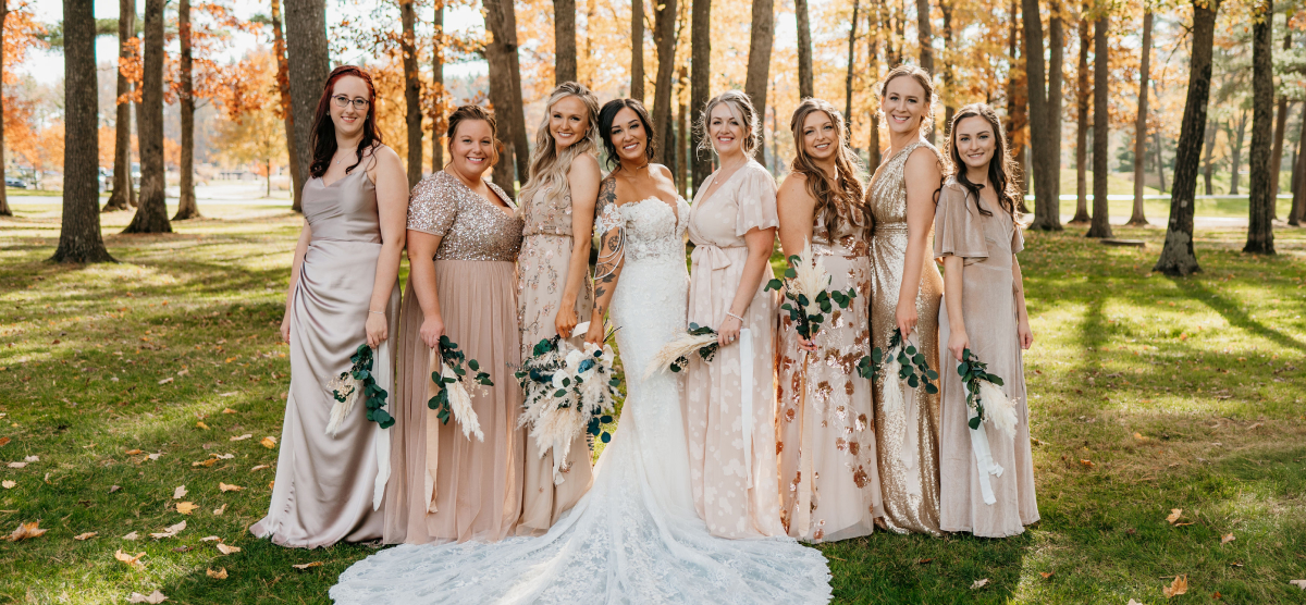 Bride and bridesmaids pose outdoors in a park with autumn trees.