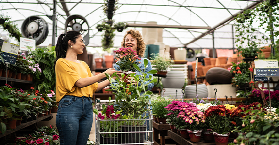 Two women adding plants to a shopping cart in a greenhouse