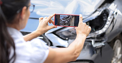 Woman taking a picture of damage to her car with her phone