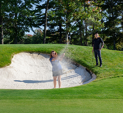 Two golfers hitting out of a sand trap at SentryWorld