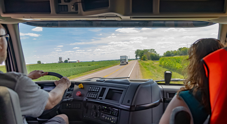 Two people sitting in the semi-truck cab driving on road