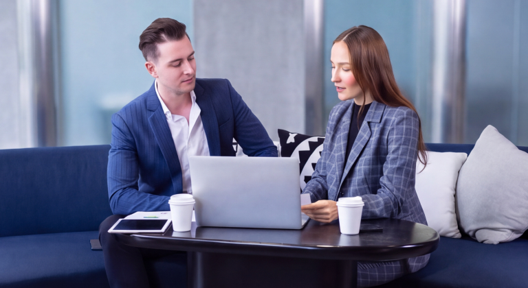 Two colleagues collaborating on a laptop in a modern office lounge.