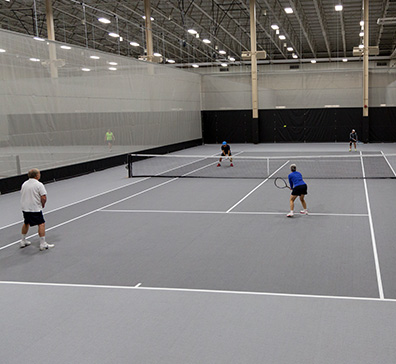 hero-fieldhouse-tennis-396x364 Fieldhouse tennis court with four people playing.