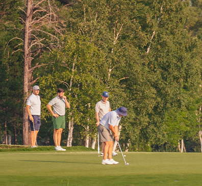 Man preparing to putt on a SentryWorld green while three friends watch on. 