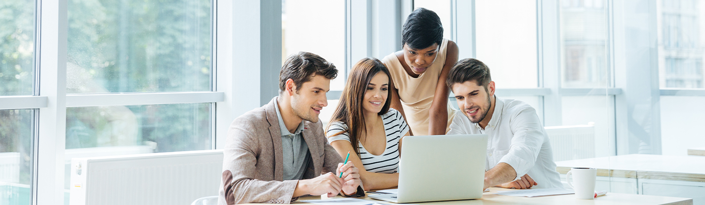 Four people in an office huddled around a laptop computer