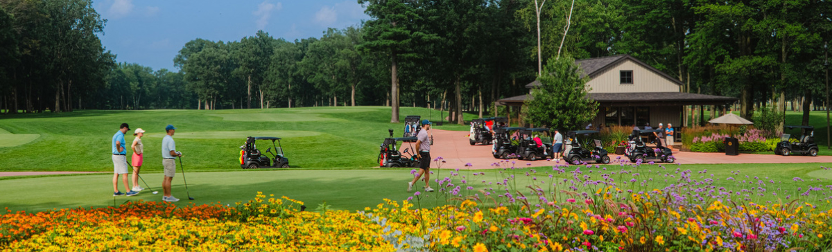 Golf group teeing off on hole one with golf carts and a refreshment station behind.