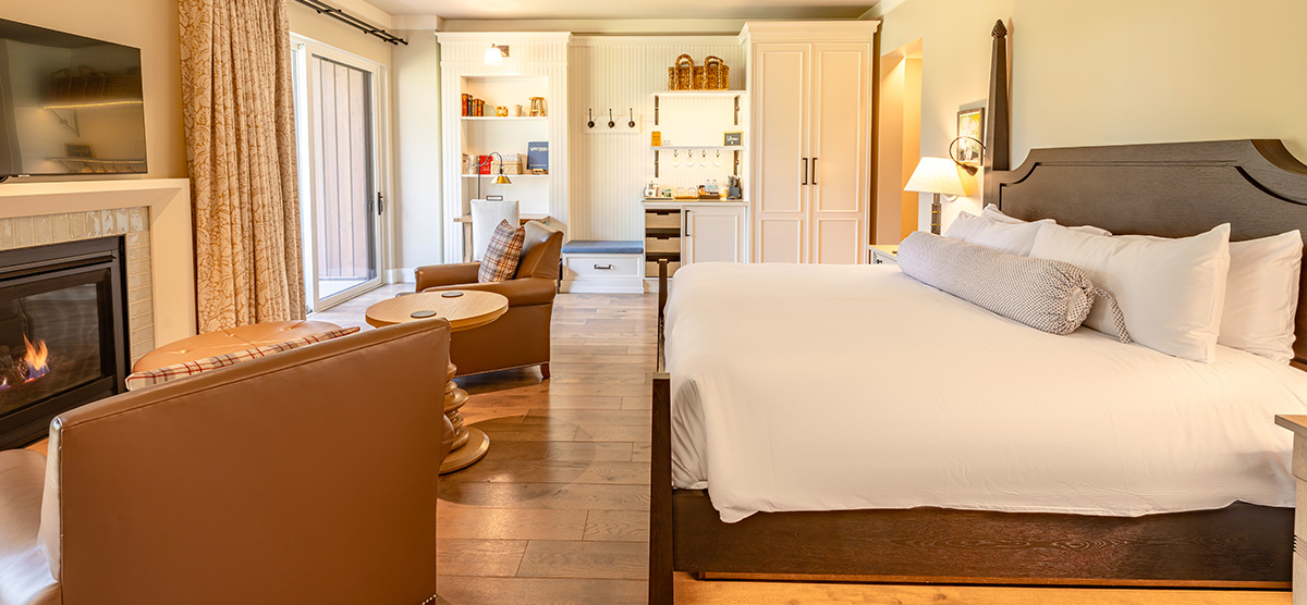 carousel-suite-golf-view-luxury-junior-4-1200x556 Hotel room with one king sized bed and two chairs in front of a fireplace.