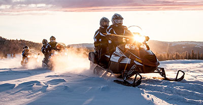 Three snowmobiles on a ride at sunrise
