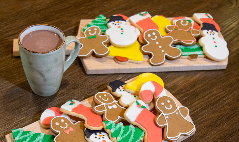 Holiday cookies on a wooden tray next to a cup of hot chocolate