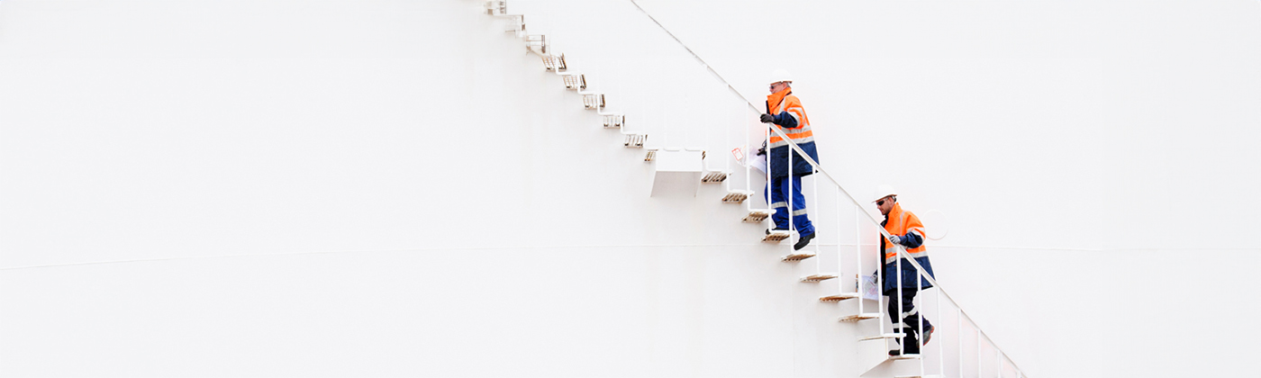 Two workers in hard hats and neon orange climbing along wall.