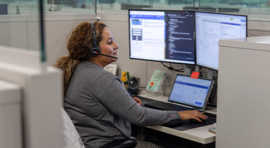 Woman talking with a customer through a headset while working on a computer.