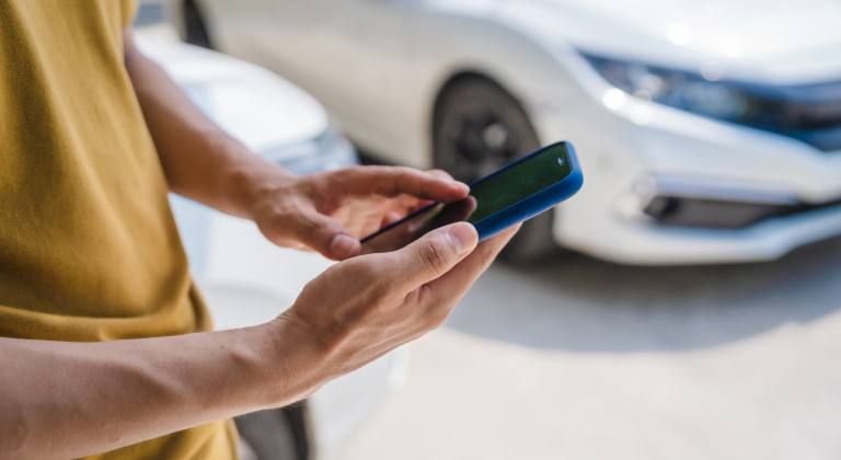 Person’s hands holding and using a smartphone outdoors, with cars in the background.