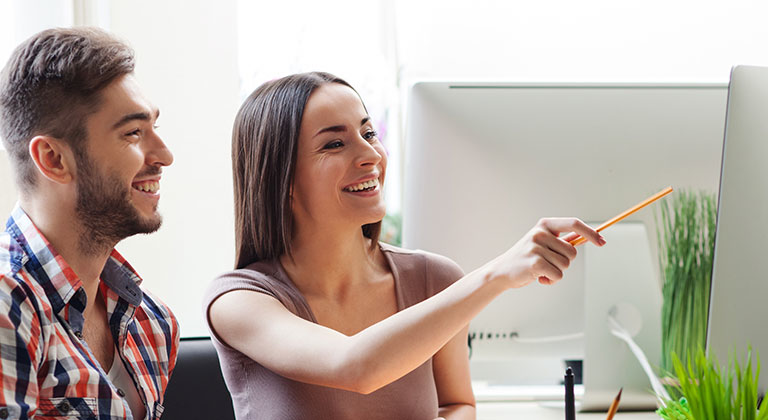 Two people smiling looking at monitor