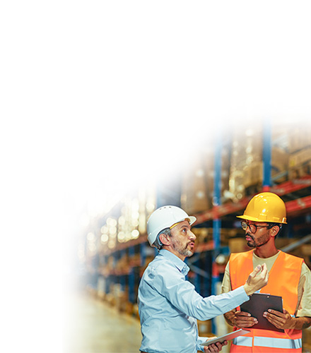 Business professional and warehouse employee wearing hard hats talking