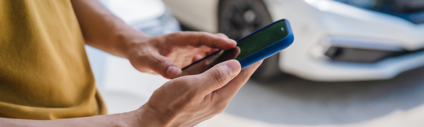 Person’s hands holding and using a smartphone outdoors, with cars in the background.