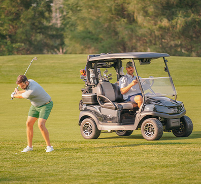 Two men golfing at SentryWorld. One is hitting his ball and the other is sitting in a golf cart. 