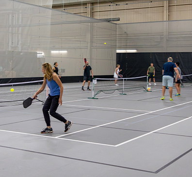 Multiple people playing pickleball on an indoor court. 