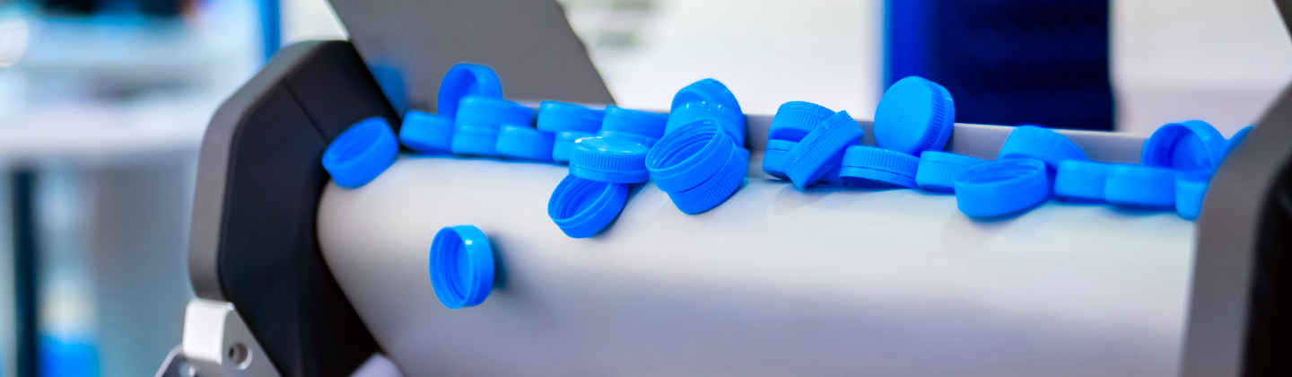 Blue plastic bottle caps moving on a conveyor belt in a factory setting.