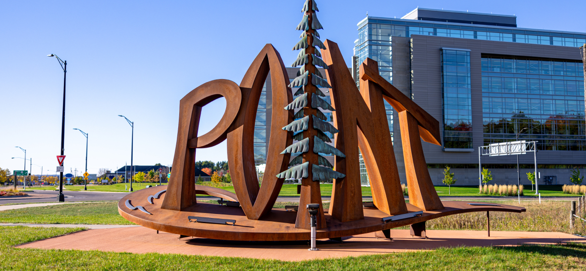 Large metal sculpture spelling ‘POINT’ with a pine tree, in front of a modern building.