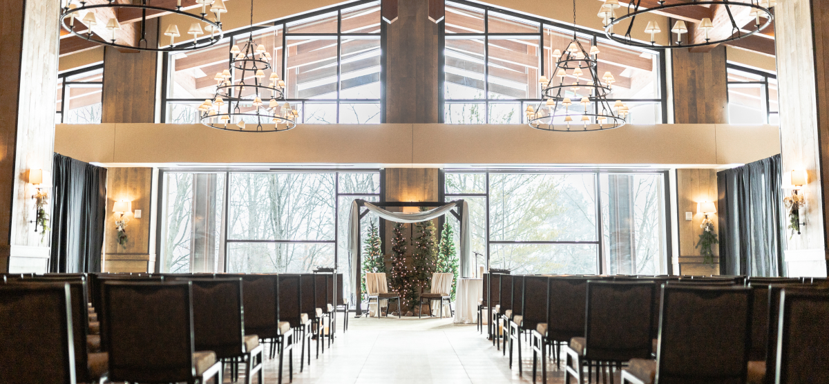 Event room set for a ceremony with rows of chairs, an archway, and large windows.