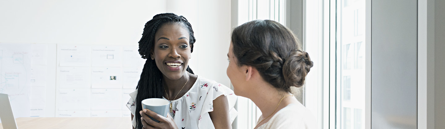 Two people talking in an office setting over coffee