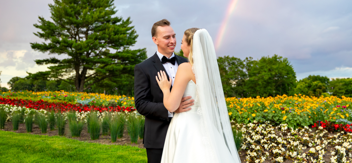 Bride and groom embrace in by the hole 16 flowers with a rainbow in the sky.