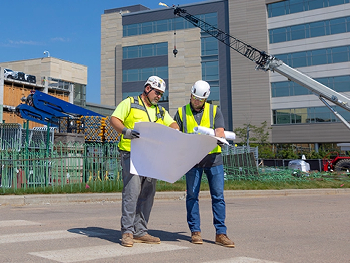 Two workers in safety helmets and hi-visibility vests working on a construction site.