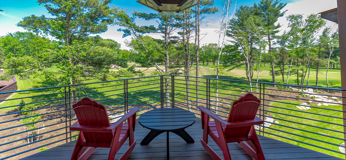 Outdoor deck chairs and a table with a golf course view in a Executive Level King Suite at The Inn