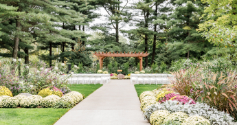 Outdoor wedding ceremony setup with white chairs and a wooden archway.