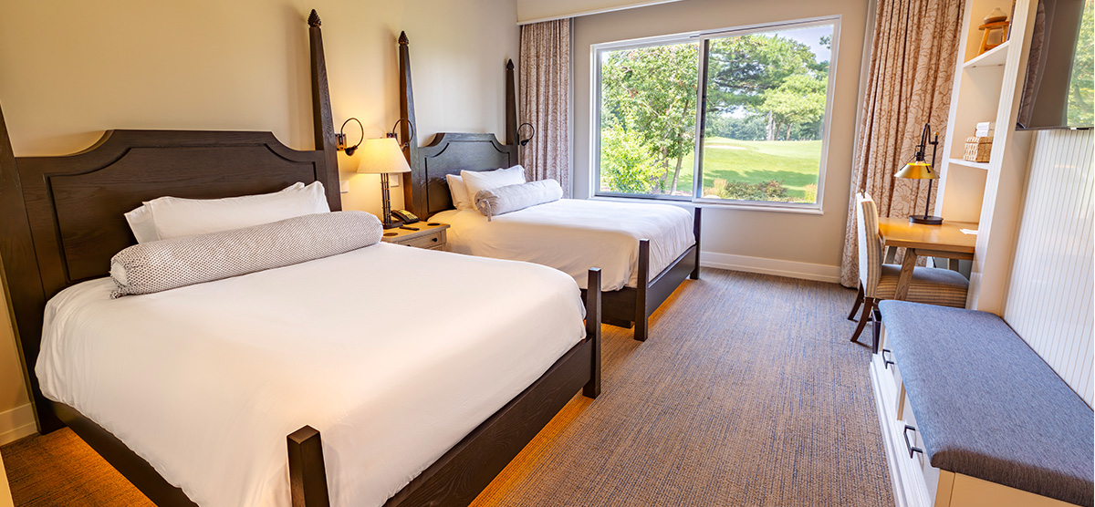 carousel-suite-golf-view-king-queen-4-1200x556 Two queen beds with desk area and bench.