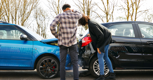 Two people looking at their cars after an accident